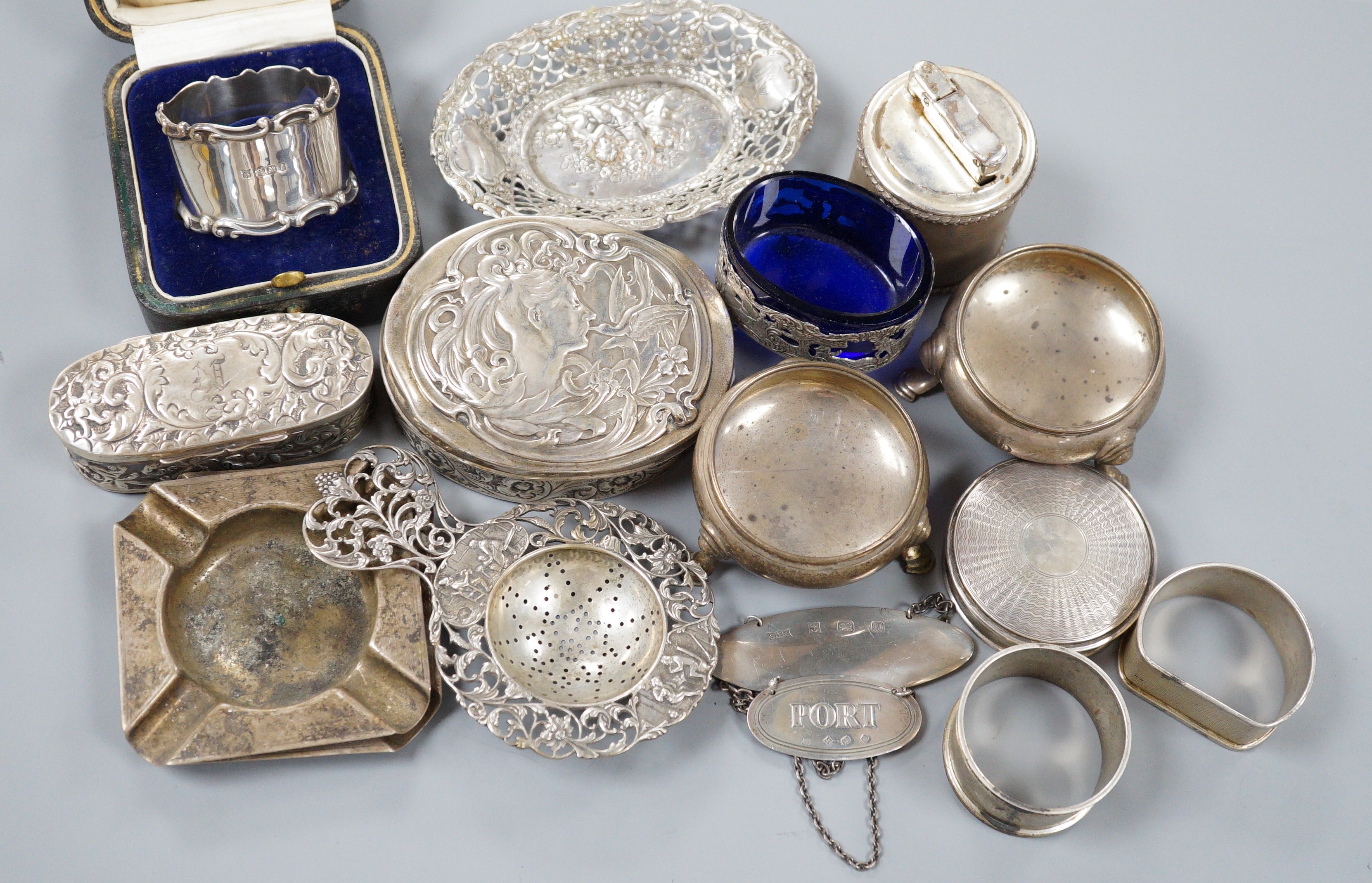 A collection of small silver items including napkin rings, repousse oval boxes, pair of bun salts, two ashtrays and a mounted table lighter, two modern wine labels, small box and three continental white metal items inclu